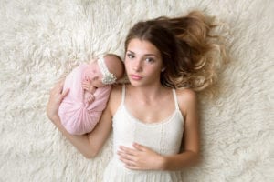 Portland Newborn Photographer big sister holding swaddled baby on rug