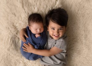 Portland Newborn Photographer Sibling holding swaddled baby on rug