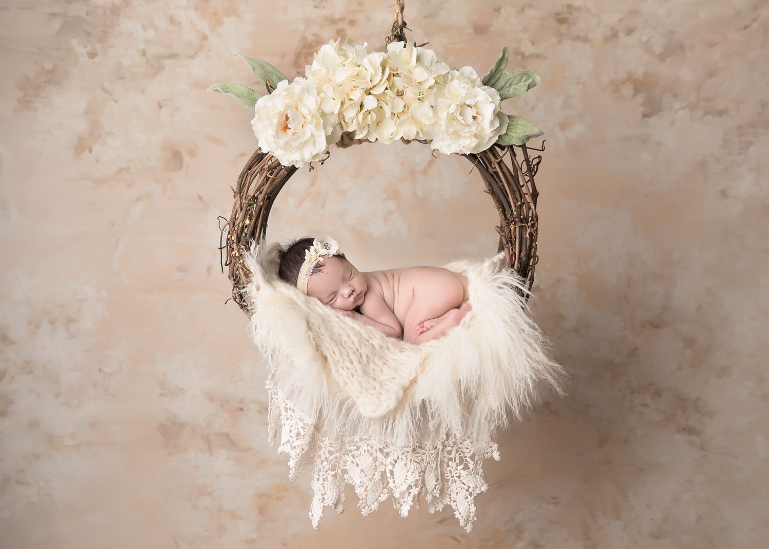 Newborn girl laying in hanging in wreath wit cream flowers on top. The background behind her is cream florals.
