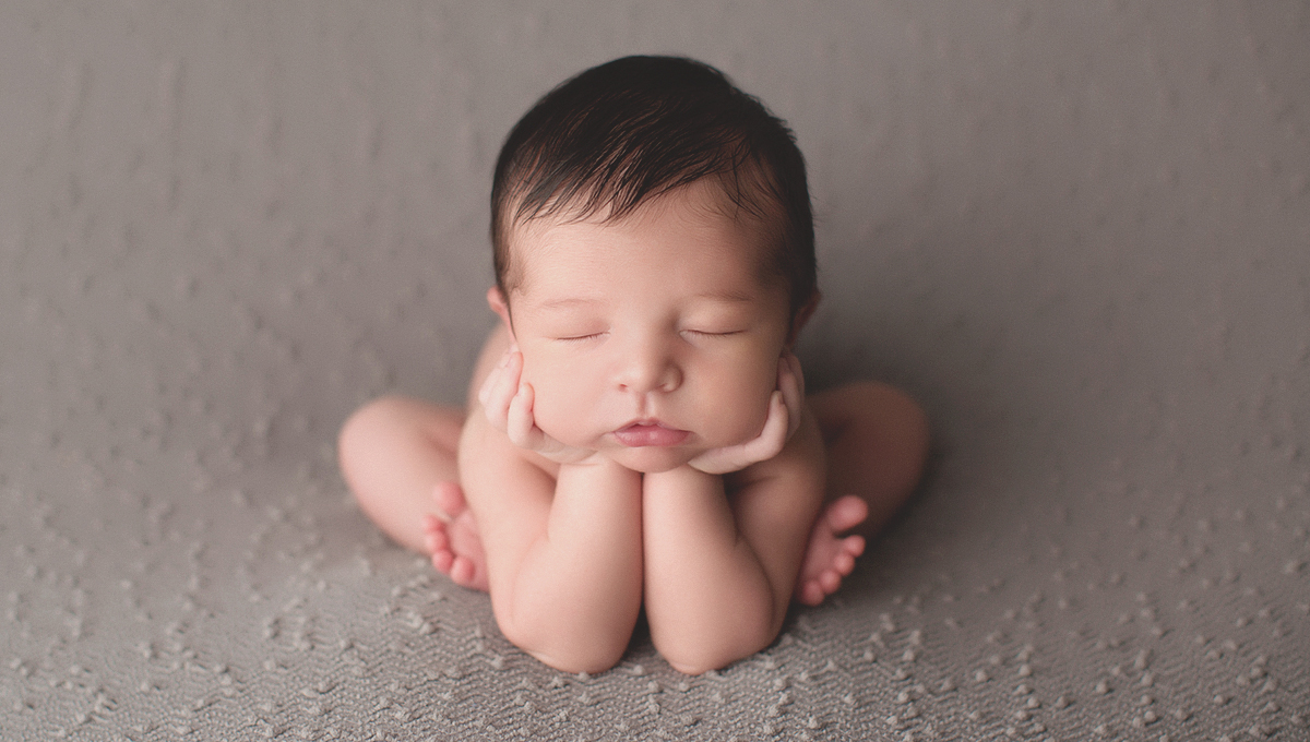 Newborn boy leaning forward in froggy pose with hands on face and toes showing in Portland studio